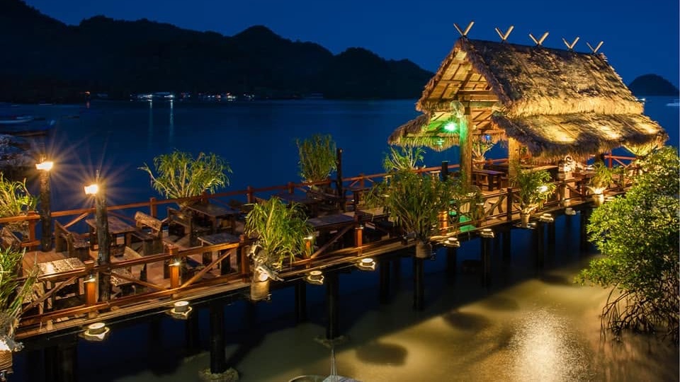 Night view of Fish Farm Restaurant’s thatched pier dining deck over Penarak water